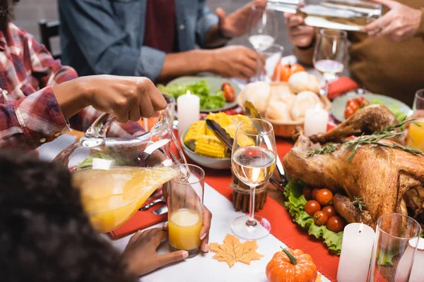 Partial view of senior man and african american woman pouring white wine and orange juice during thanksgiving dinner with multicultural family — Stock Photo