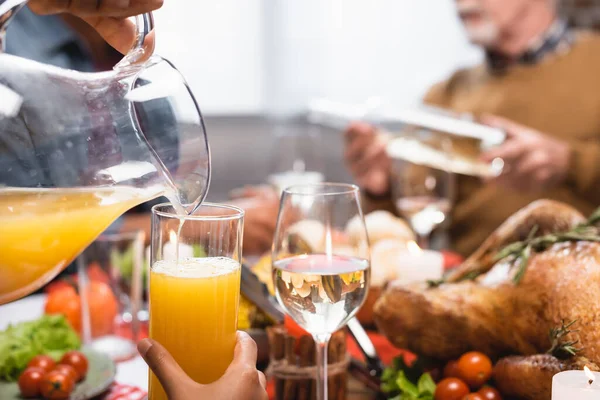 Vista recortada de la mujer afroamericana vertiendo jugo de naranja durante la cena de acción de gracias - foto de stock