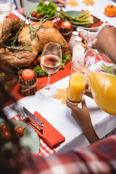 Vista recortada de la hija afroamericana sosteniendo vidrio mientras la madre vierte jugo de naranja durante la cena de acción de gracias - foto de stock