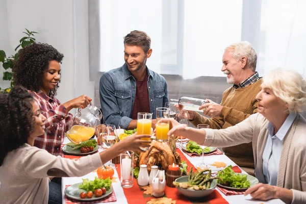 Multicultural family clinking glasses with beverages during celebration of thanksgiving day — Stock Photo