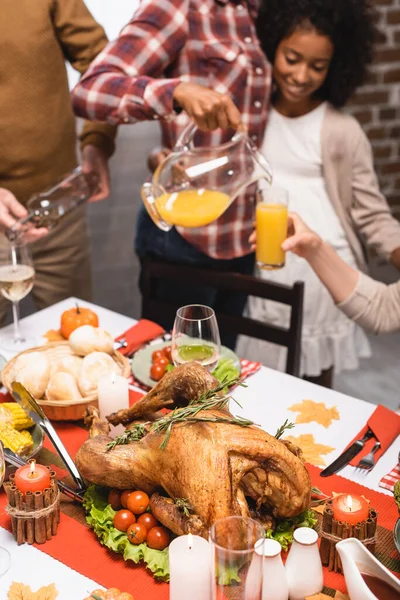 Vista recortada de la familia multicultural que vierte bebidas en la mesa servida con deliciosa cena de acción de gracias - foto de stock