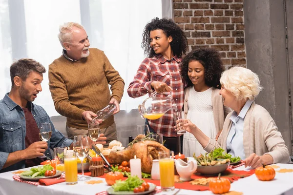 Gioioso uomo africano americano e donna anziana che si guardano mentre versano bevande durante la cena del Ringraziamento — Foto stock