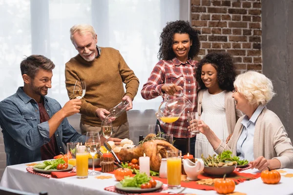 Senior man and african american woman pouring beverages during thanksgiving dinner with multicultural family — Stock Photo