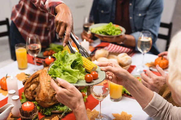 Vista ritagliata della donna anziana che tiene il piatto con le verdure durante la cena del Ringraziamento con famiglia multiculturale — Foto stock