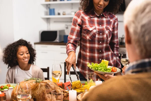African american woman serving vegetables while celebrating thanksgiving day with multicultural family — Stock Photo