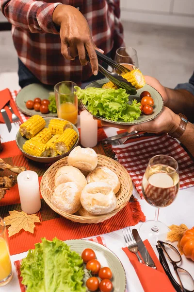 Vue recadrée de femme afro-américaine mettant des légumes dans l'assiette tout en célébrant le jour de l'Action de grâces — Photo de stock