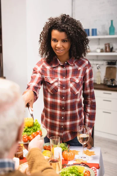 Homem sênior segurando prato com legumes perto de mulher americana africana durante o jantar de ação de graças — Fotografia de Stock