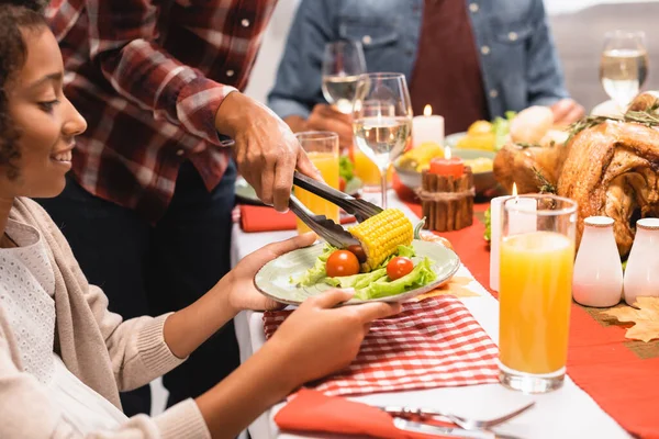 Selektiver Fokus der afrikanisch-amerikanischen Frau, die Mais auf Teller für Tochter während des Erntedankmahls legt — Stockfoto