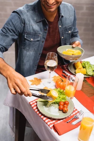 Vista ritagliata dell'uomo che prende mais vicino a verdure fresche, bevande e zucca decorativa mentre celebra il giorno del Ringraziamento — Foto stock