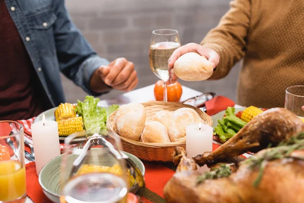 Vista cortada do homem sênior segurando pão enquanto sentado perto do filho na mesa com jantar de ação de graças — Fotografia de Stock