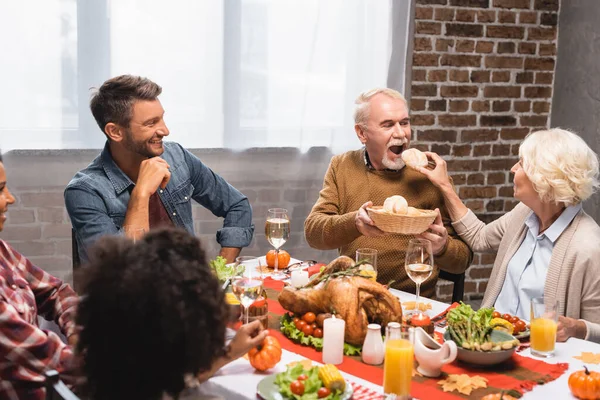 Donna anziana che alimenta l'uomo con panino vicino alla famiglia multiculturale durante la cena del Ringraziamento — Foto stock