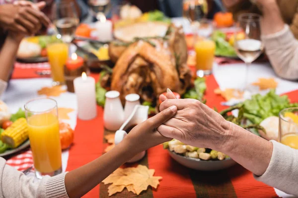 Vista cortada de família interracial sentado à mesa e de mãos dadas — Fotografia de Stock