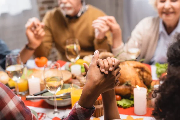 Abgeschnittene Ansicht einer multikulturellen Familie, die sich beim Danksagungsessen Händchen haltend betet — Stockfoto