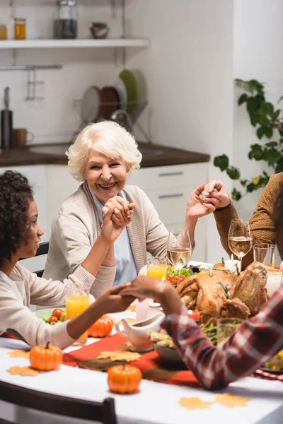 Selective focus of senior woman looking at african american girl while holding hands on thanksgiving — Stock Photo