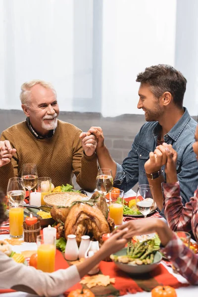Erfreut multikulturelle Familie Händchen haltend beim Abendessen zum Erntedankfest — Stockfoto