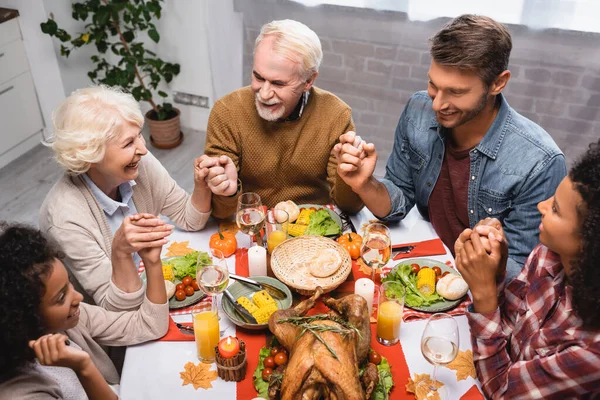 Vista ad alto angolo della famiglia multietnica che si tiene per mano e celebra il Ringraziamento a casa — Foto stock