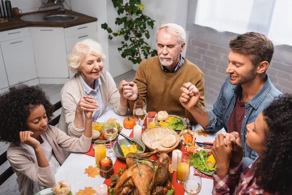 Багатоетнічна сім'я з закритими очима тримає руки і святкує подяку вдома — стокове фото
