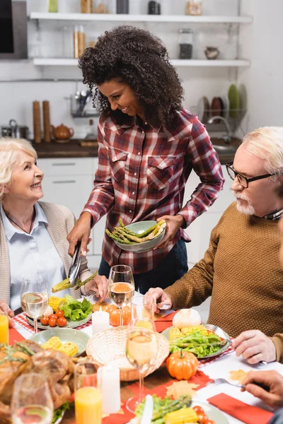 Femme afro-américaine servant des asperges près de la femme âgée pendant le dîner de Thanksgiving — Photo de stock