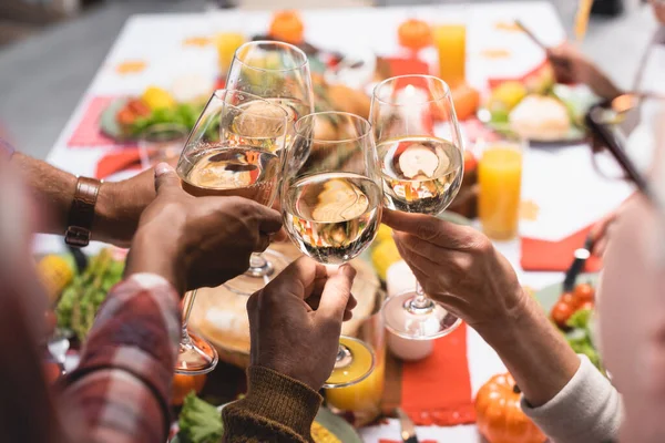 Vista parcial de parientes multiétnicos tintineando copas de vino mientras celebran el día de acción de gracias - foto de stock