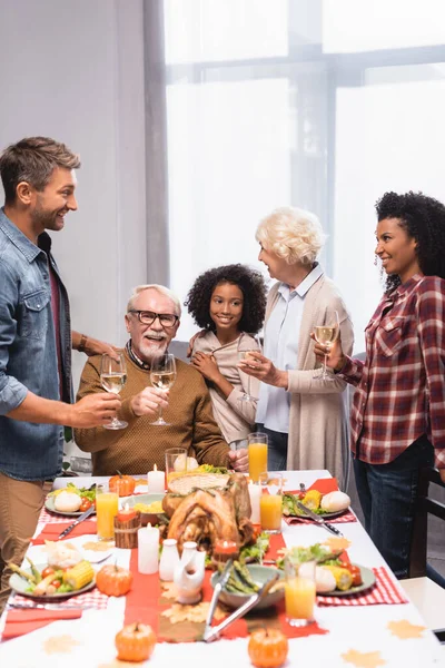 Gioiosa famiglia multiculturale che tiene bicchieri di vino mentre celebra il giorno del ringraziamento — Foto stock
