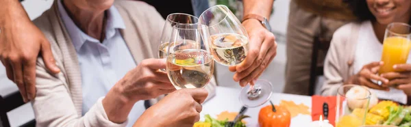 Cropped view of multiethnic family clinking wine glasses while celebrating thanksgiving, panoramic shot — Stock Photo