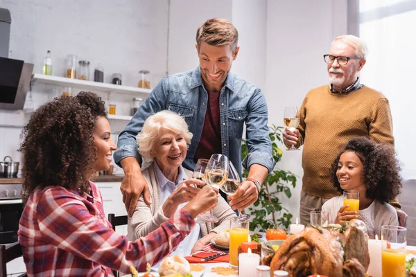 Familia multiétnica emocionada tintineo copas de vino durante la cena de acción de gracias — Stock Photo