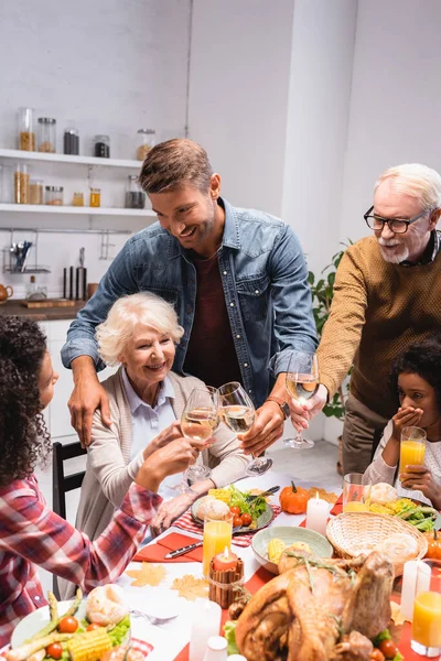 Foco seletivo da família multiétnica clinking com vinho durante a celebração de ação de graças — Fotografia de Stock