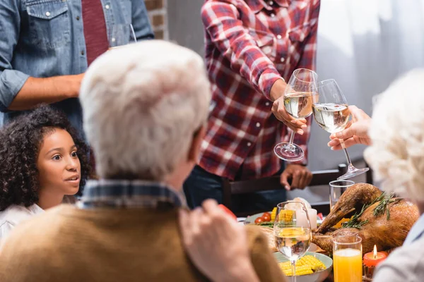 Enfoque selectivo de las mujeres brindando con vino durante la celebración de la acción de gracias con la familia multiétnica - foto de stock