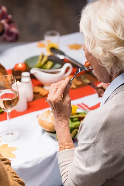 Concentration sélective de la femme âgée mangeant de la tomate cerise près du dîner d'Action de grâces — Photo de stock