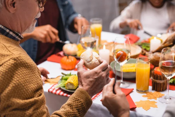Selective focus of senior man holding bun during thanksgiving dinner with family at home — Stock Photo