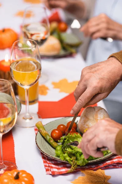 Обрезанный вид пожилого человека, поедающего салат рядом с женой и праздничный ужин — стоковое фото
