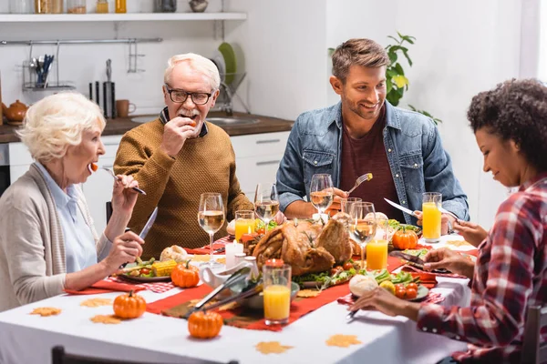 El foco selectivo de la familia multicultural con la hija celebrando el Día de Acción de Gracias cerca de la comida sabrosa en la mesa - foto de stock