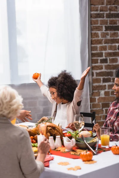 Focus selettivo della ragazza afro-americana che tiene la zucca vicino ai genitori durante la cena del Ringraziamento — Foto stock