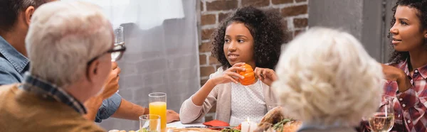 Orientation panoramique de la fille afro-américaine tenant la citrouille près des parents et dîner d'action de grâce — Photo de stock