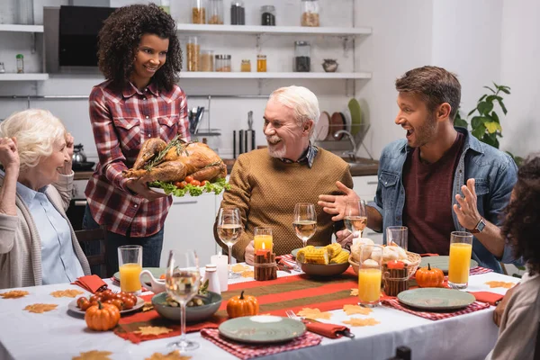 Selective focus of african american woman holding turkey near family at table in kitchen — Stock Photo