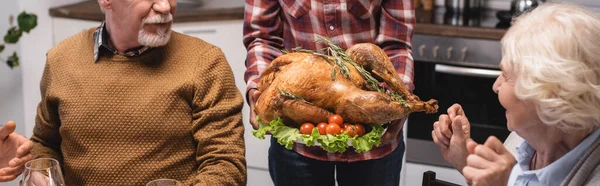 Panoramic shot of woman holding tasty turkey near family in kitchen — Stock Photo