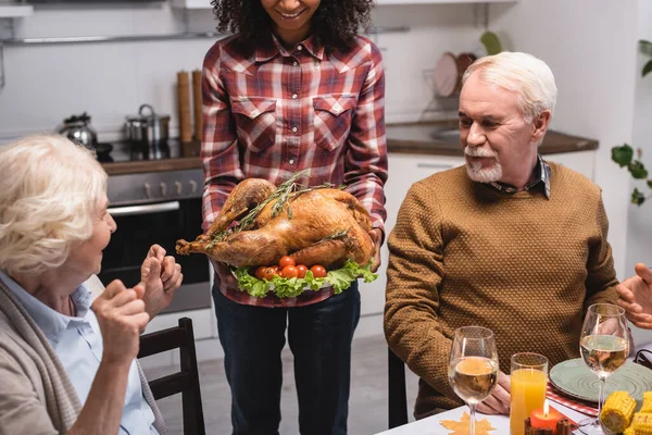 Focus selettivo della donna afro-americana che tiene il tacchino vicino alla famiglia multietnica in cucina — Foto stock