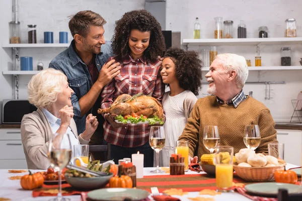 Selective focus of african american woman holding turkey near family during thanksgiving celebration — Stock Photo