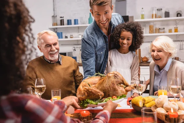 Focus selettivo dell'uomo guardando la fotocamera vicino alla famiglia multietnica e la cena di ringraziamento con arredamento sul tavolo — Foto stock