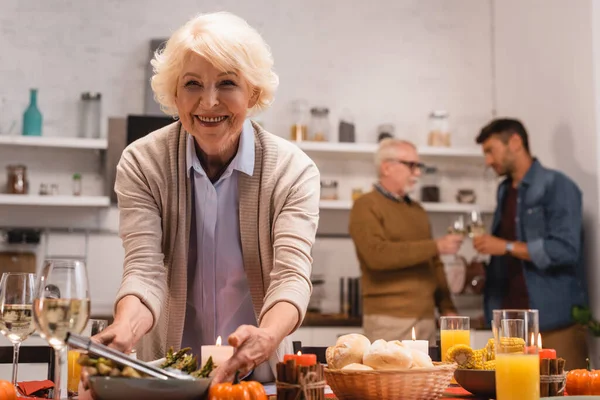 Selektiver Fokus einer älteren Frau, die beim Erntedankessen neben leckerem Essen und Kerzen auf dem Tisch steht — Stockfoto