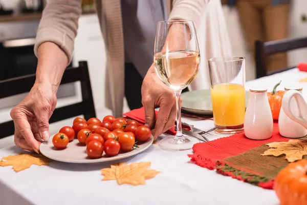 Vista ritagliata della donna anziana che mette pomodori ciliegia sul tavolo vicino a foglie e zucche autunnali — Foto stock