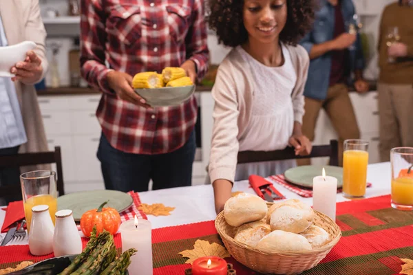 Селективный фокус африканской американки, держащей корзину с булочками рядом с родителями во время праздничного ужина — стоковое фото