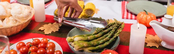 Eine afrikanisch-amerikanische Frau mit Pinzette in der Nähe von Spargel und Kerzen auf dem Tisch während des Erntedankfestes — Stockfoto