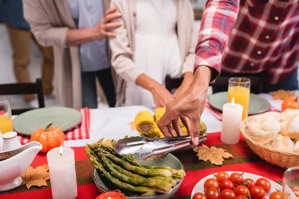 Cropped view of african american woman holding tweezers near food during thanksgiving celebration — Stock Photo