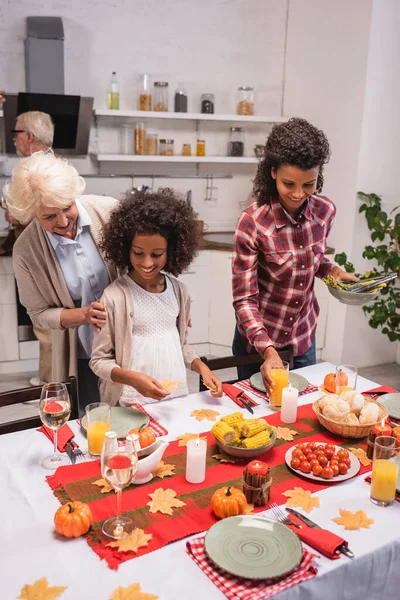 Selective focus of elderly woman embracing african american granddaughter near thanksgiving dinner — Stock Photo