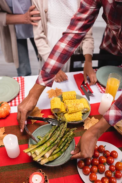 Cropped view of african american woman putting asparagus on table during thanksgiving dinner — Stock Photo