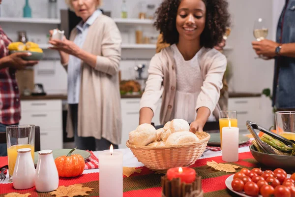 Selective focus of african american kid holding basket with buns near parents during thanksgiving dinner — Stock Photo