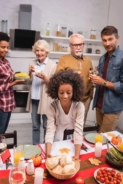 Selective focus of african american kid holding basket with buns near parents during thanksgiving dinner — Stock Photo