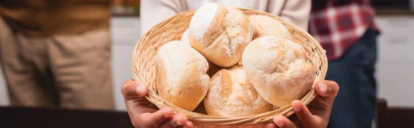 Panoramic crop of african american child holding basket with buns at home — Stock Photo