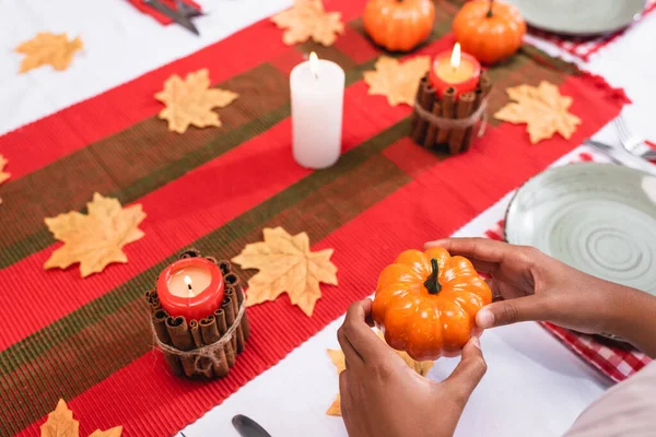 Vista recortada de un niño afroamericano sosteniendo calabaza decorativa cerca de velas en la mesa durante el día de acción de gracias - foto de stock
